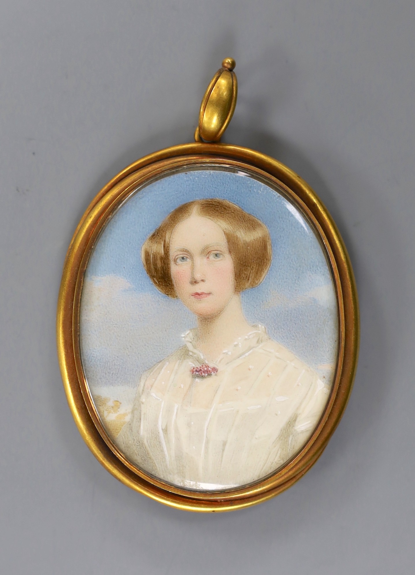 A yellow metal mounted oval portrait miniature of a young lady pendant miniature, the glazed back with plated hair beneath, 67mm, gross weight 42.7 grams.